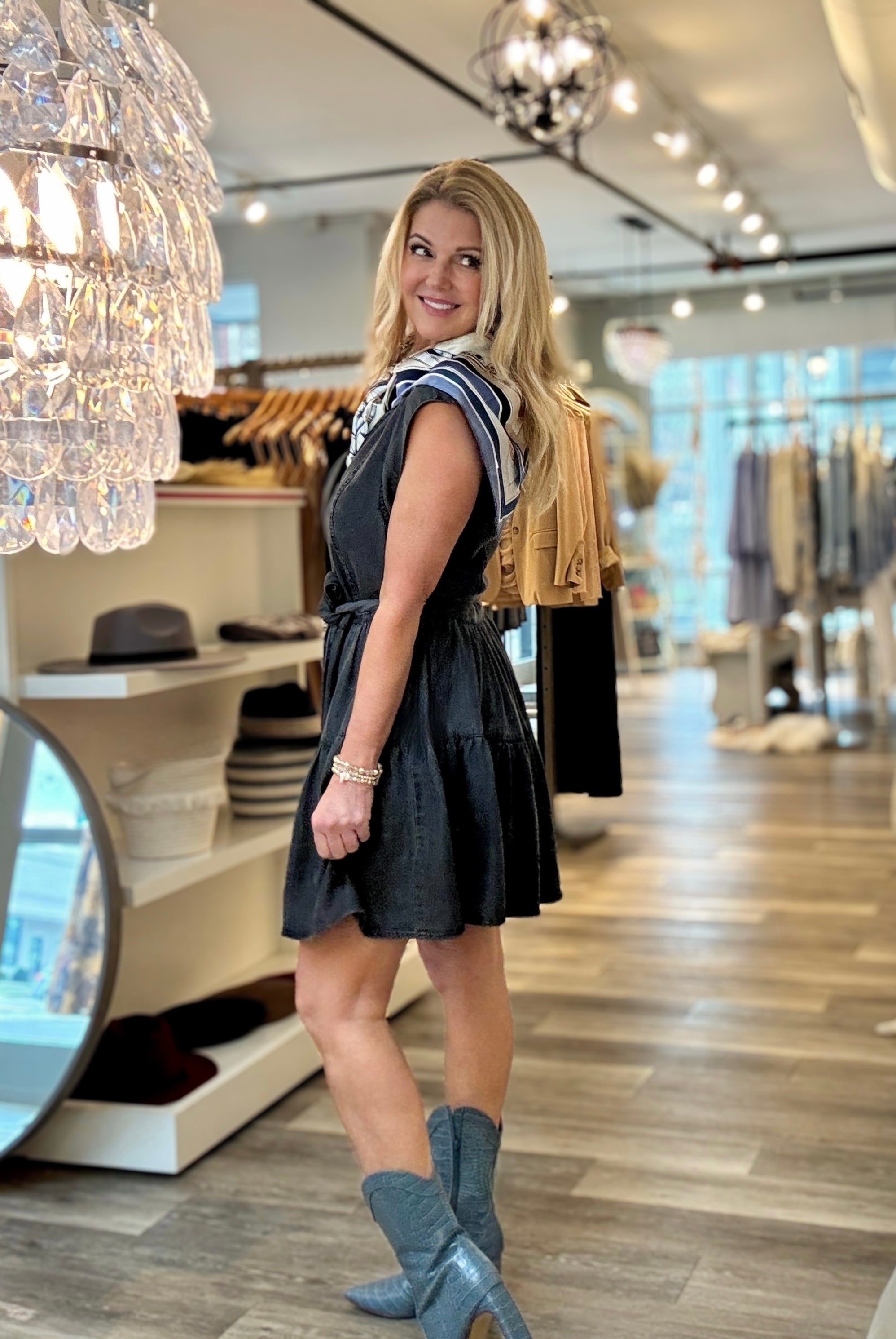 side view of the Black washed denim dress with tie waist in Mainstream Boutique Bloomington with boots.