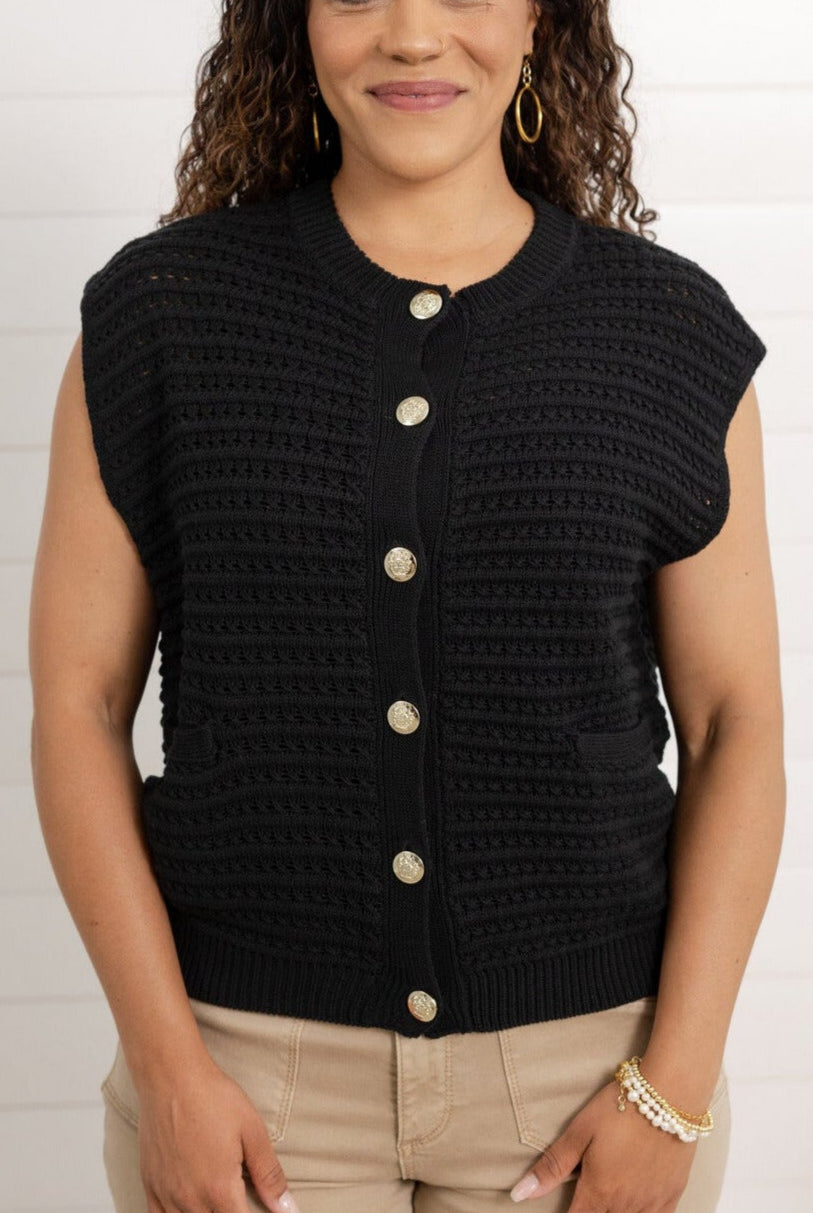 Woman wearing a black sleeveless textured top with buttons against a white background