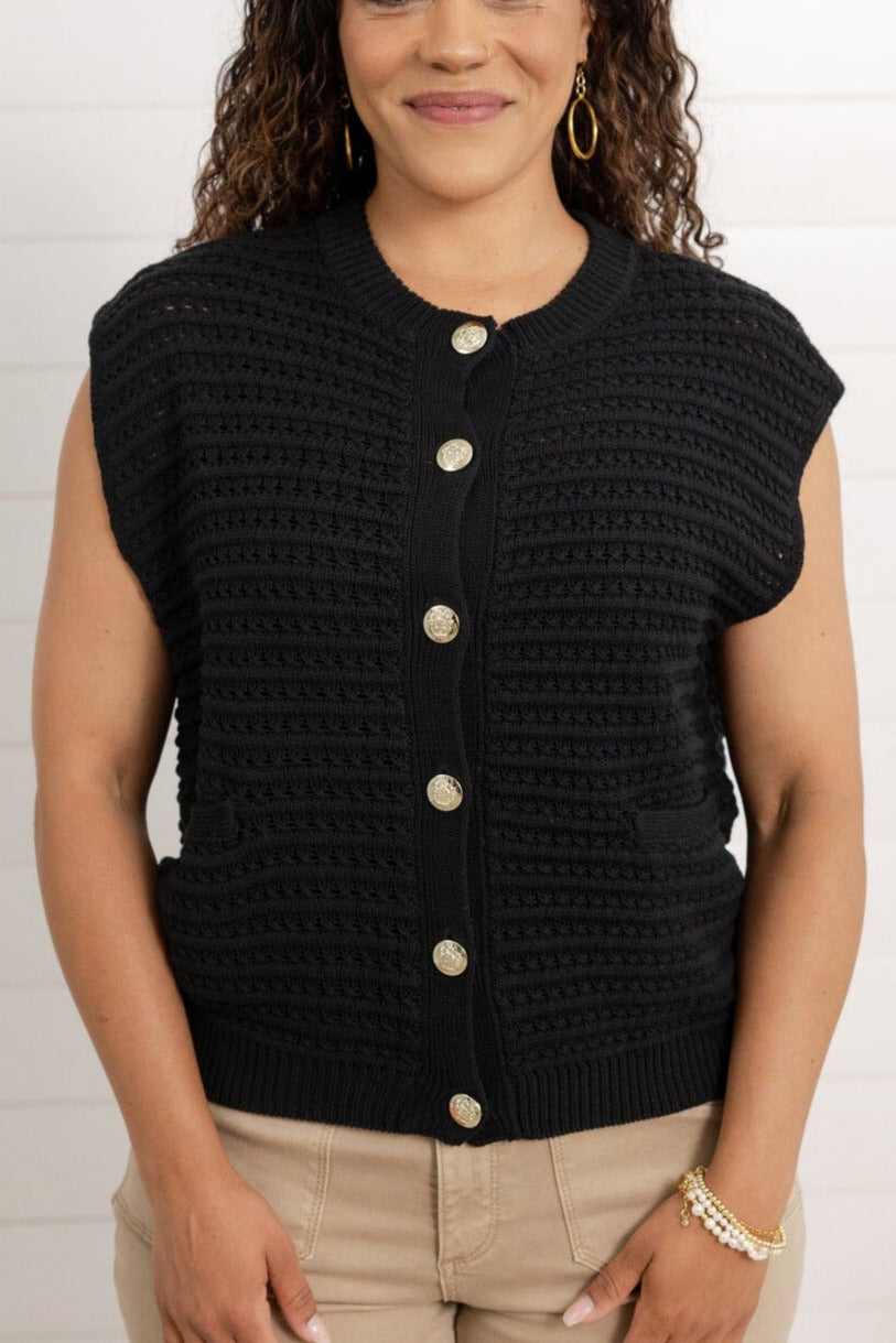 Woman wearing a black sleeveless textured top with buttons against a white background