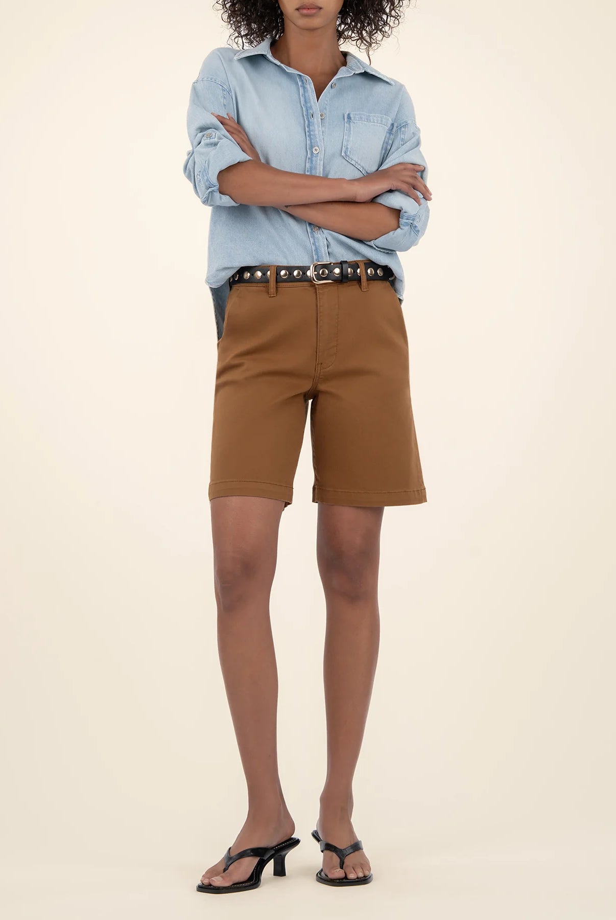Person wearing a light blue shirt and brown shorts on a beige background