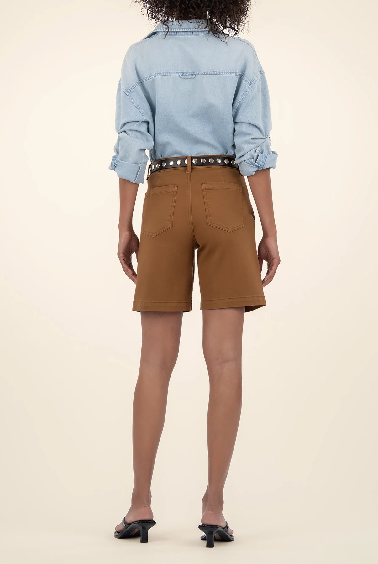 Person wearing a light blue denim shirt and brown shorts on a beige background