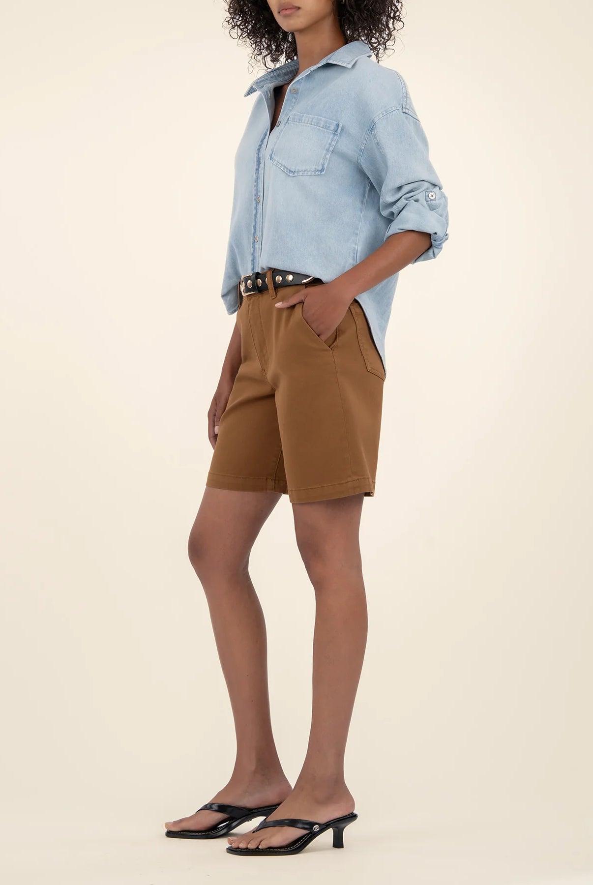 Person wearing a light blue denim shirt and brown shorts on a beige background