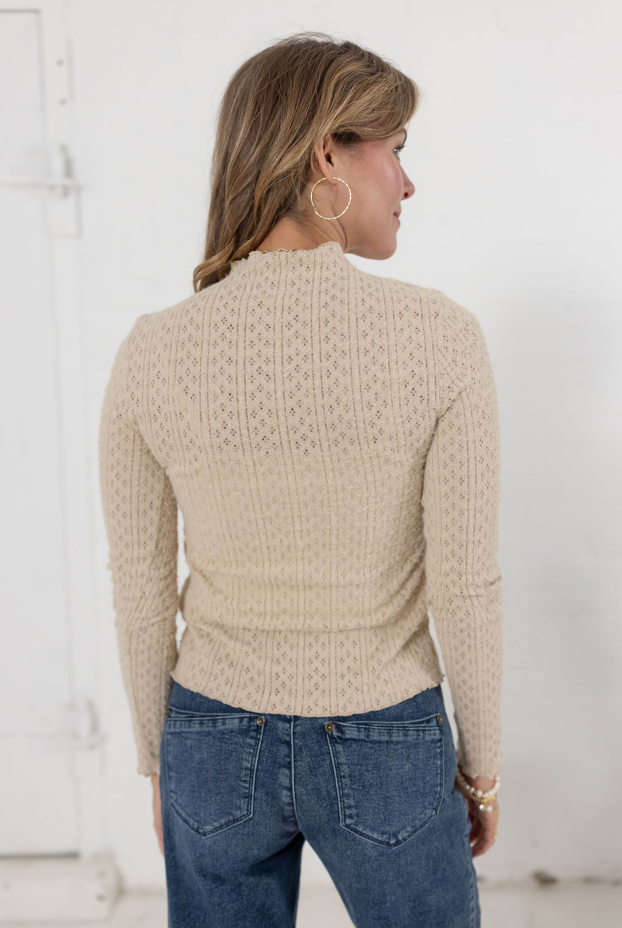 woman showing the back of the lettuce edge detail mock neck top in the color almond