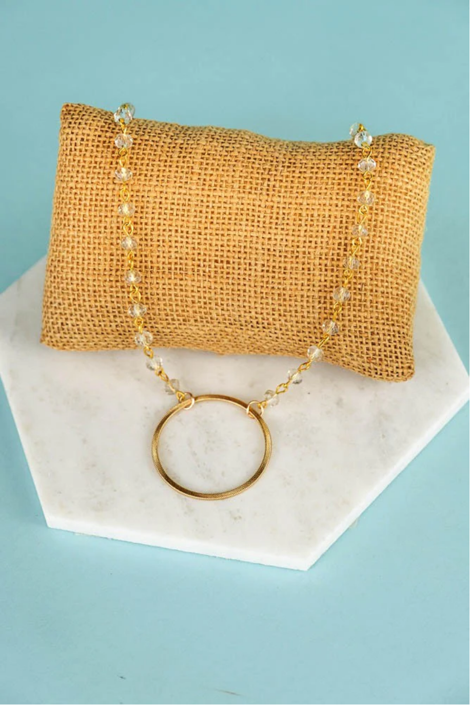 A gold-colored necklace displayed on a white marble surface with a textured gold-colored pendant.