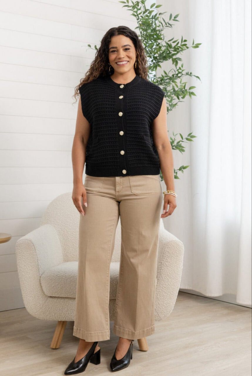 Woman wearing a black textured sweater vest with tan pants.