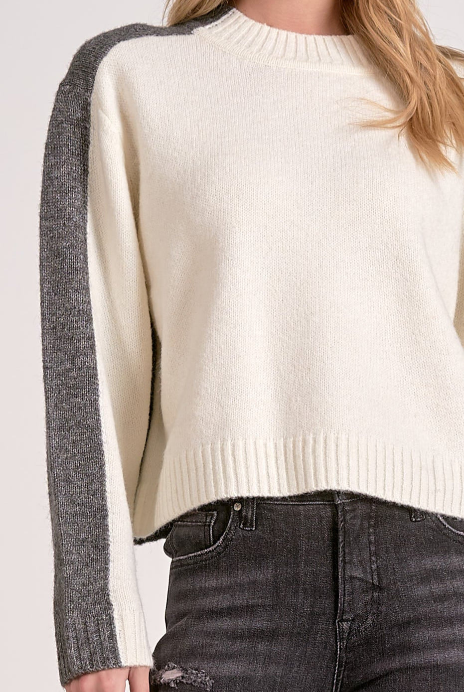 Woman showing the details on the white and grey color block crewneck sweater with soft knit and stripe sleeve effect