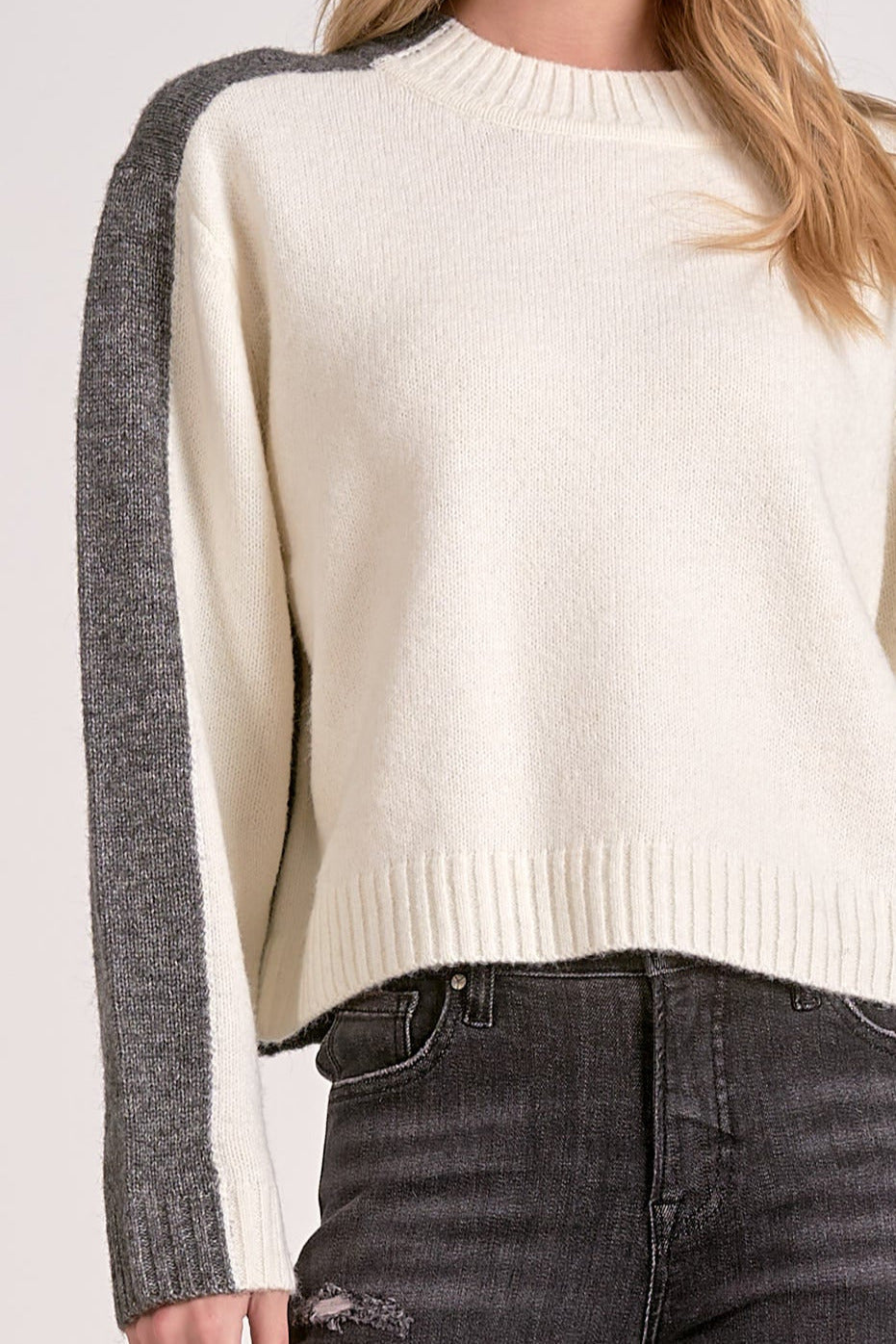 Woman showing the details on the white and grey color block crewneck sweater with soft knit and stripe sleeve effect