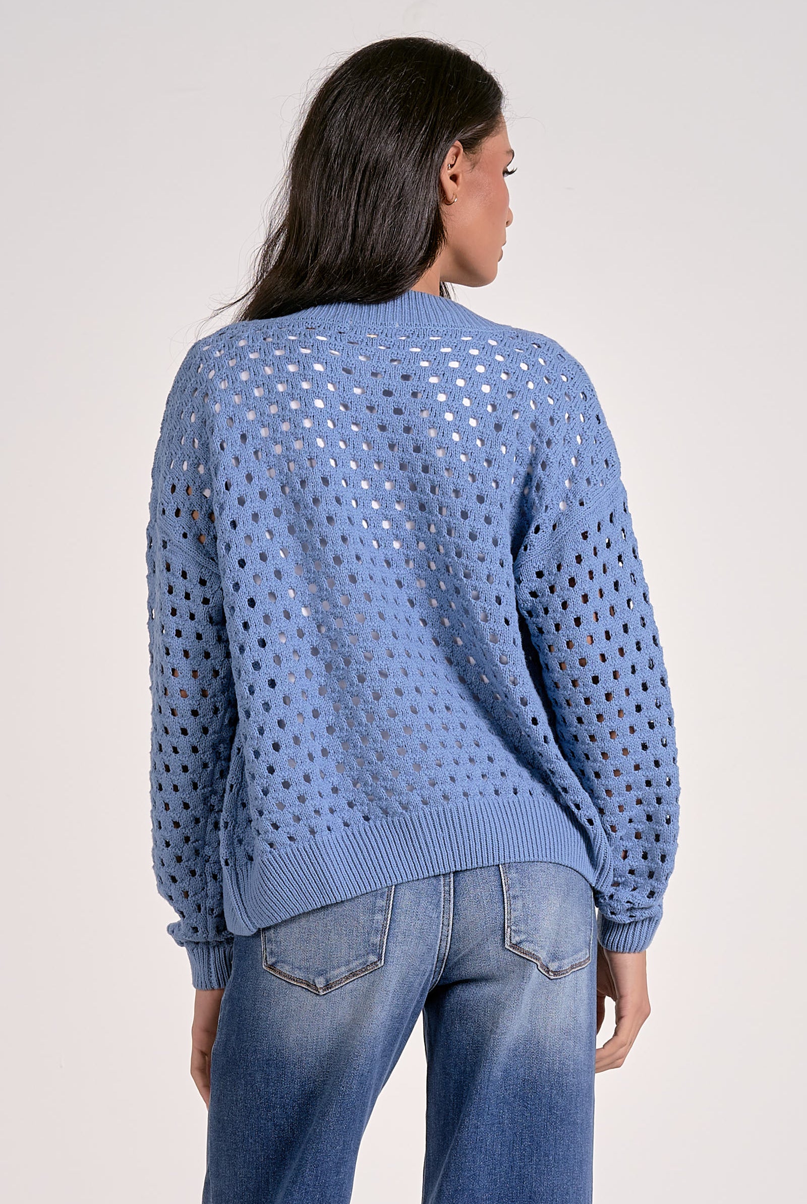 Woman showing the back of the soft blue open-knit zip cardigan layered over a white top.