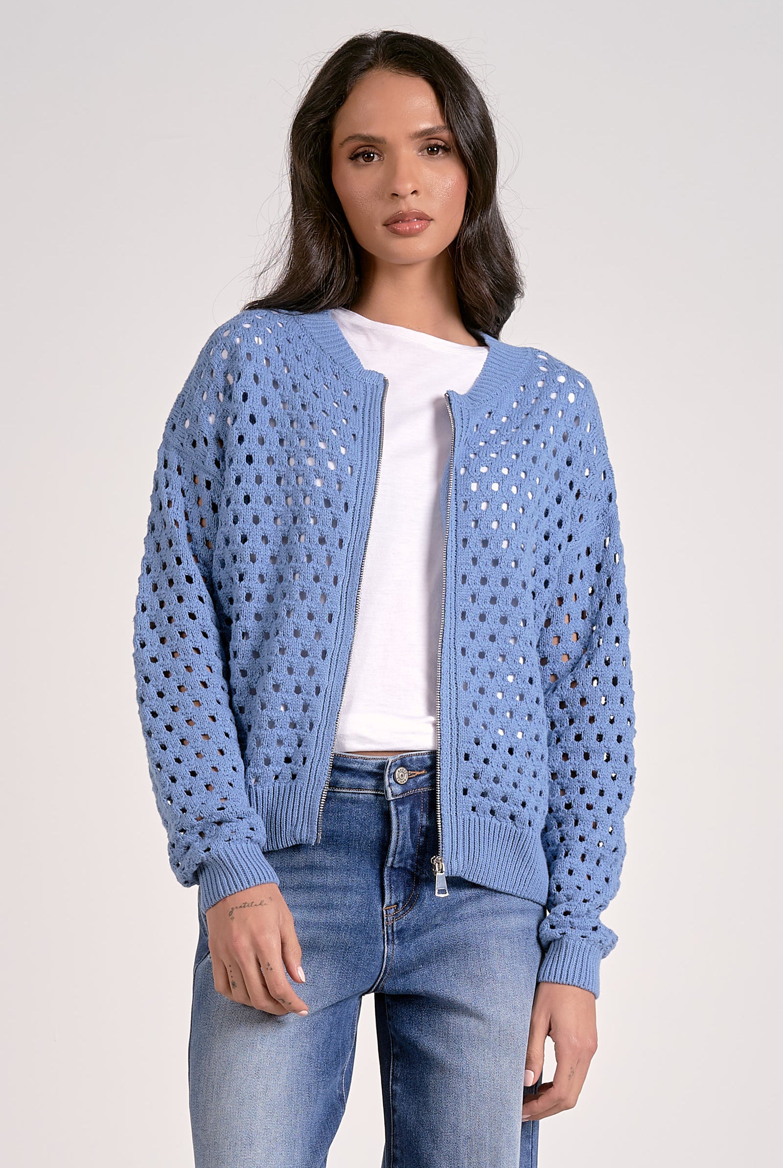 Woman wearing a soft blue open-knit zip cardigan layered over a white top