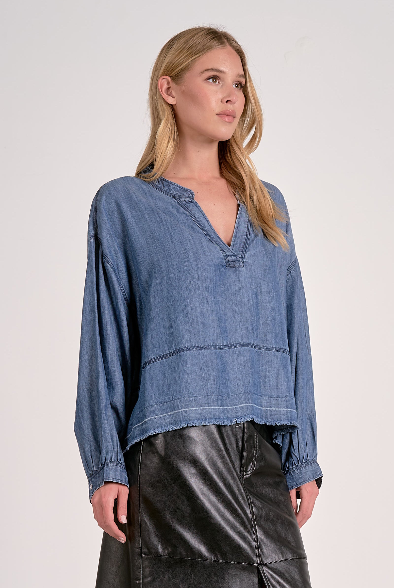 Woman wearing washed denim V-neck pullover with long sleeves, frayed hem, and relaxed fit