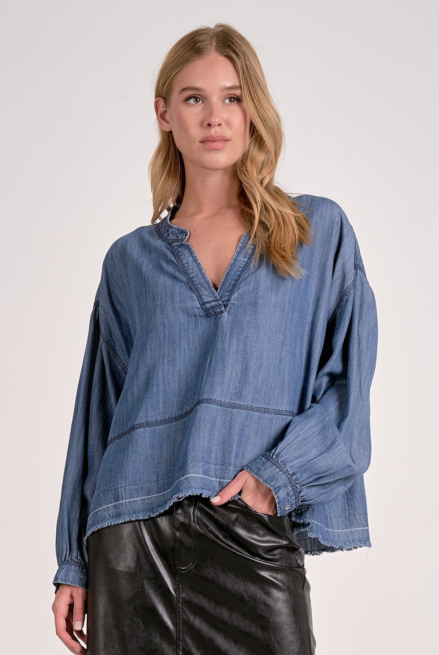 Front view of a woman wearing a washed denim V-neck pullover showing long sleeves, relaxed fit, and frayed hem