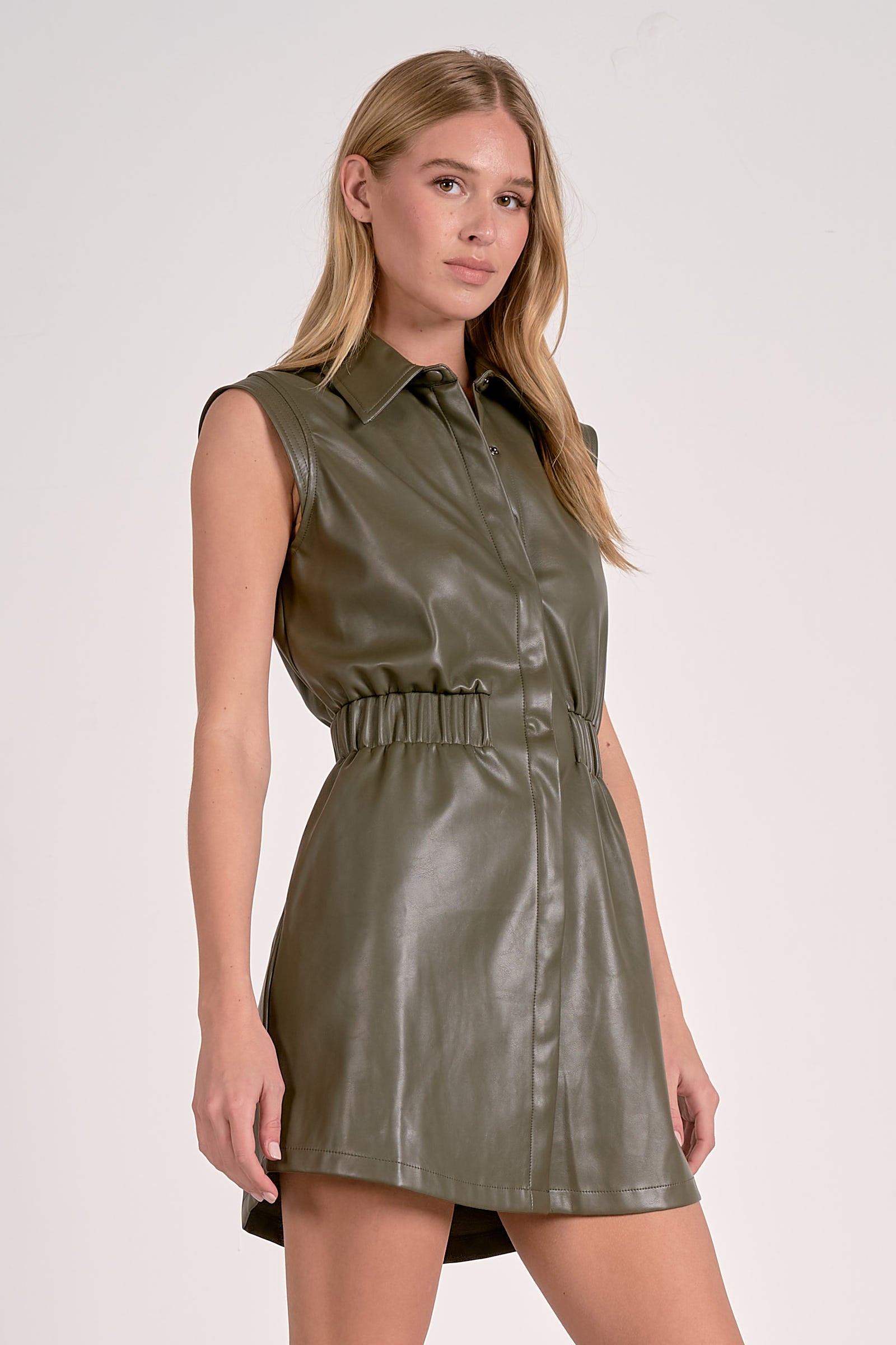 woman showing the side of the pine color faux leather elastic waist short dress with collared neckline and snap front