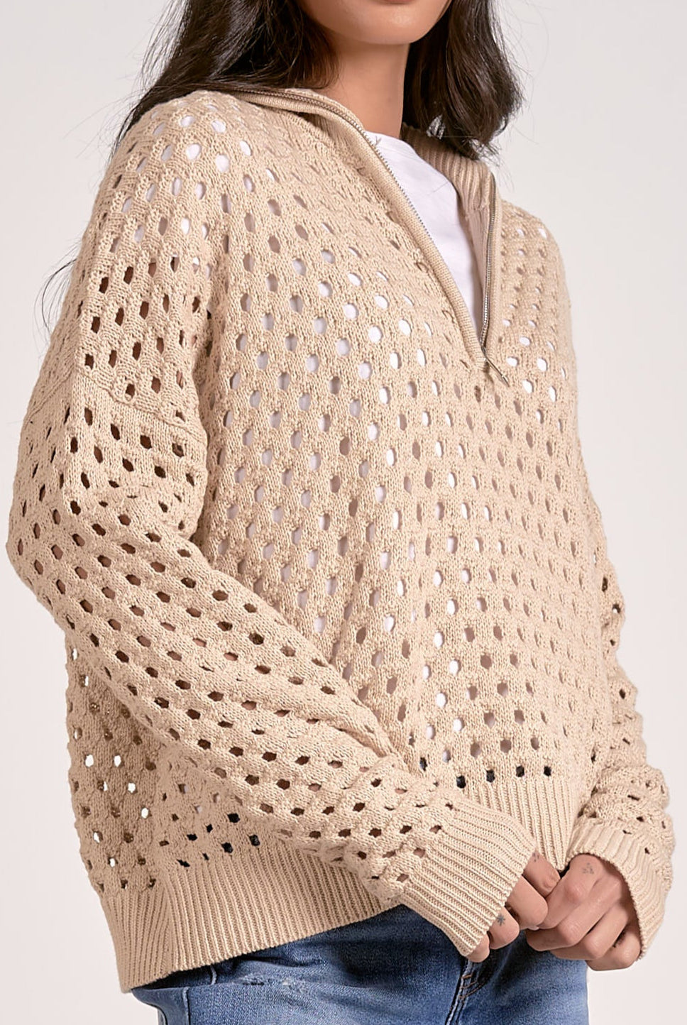 Woman wearing a lightweight oatmeal half zip open knit sweater with ribbed cuffs and hem, styled with denim jeans.
