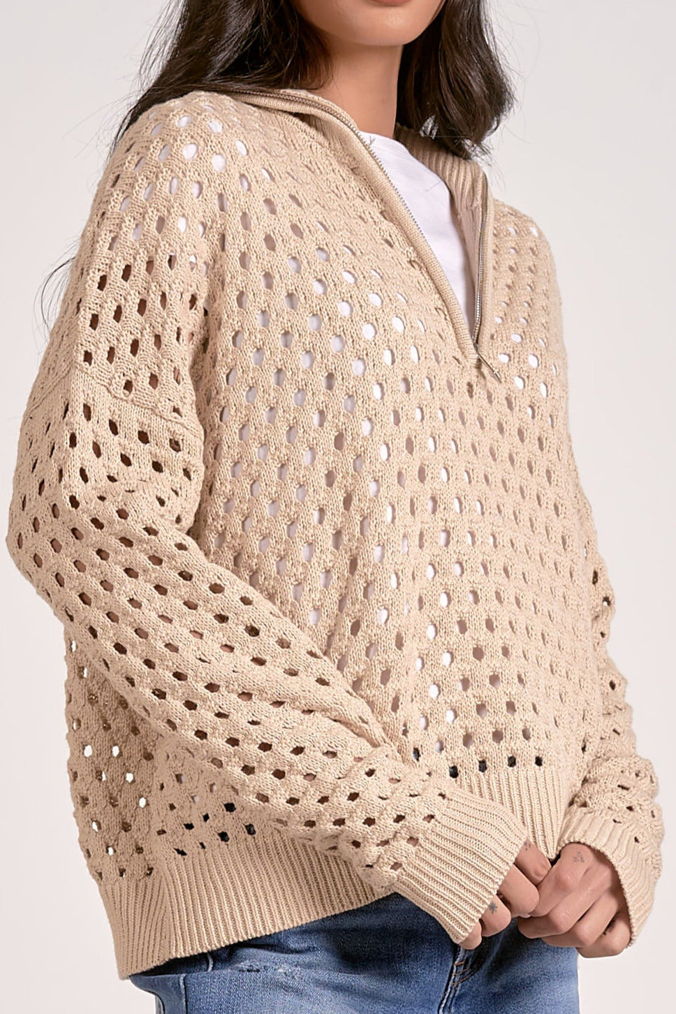 Woman wearing a lightweight oatmeal half zip open knit sweater with ribbed cuffs and hem, styled with denim jeans.
