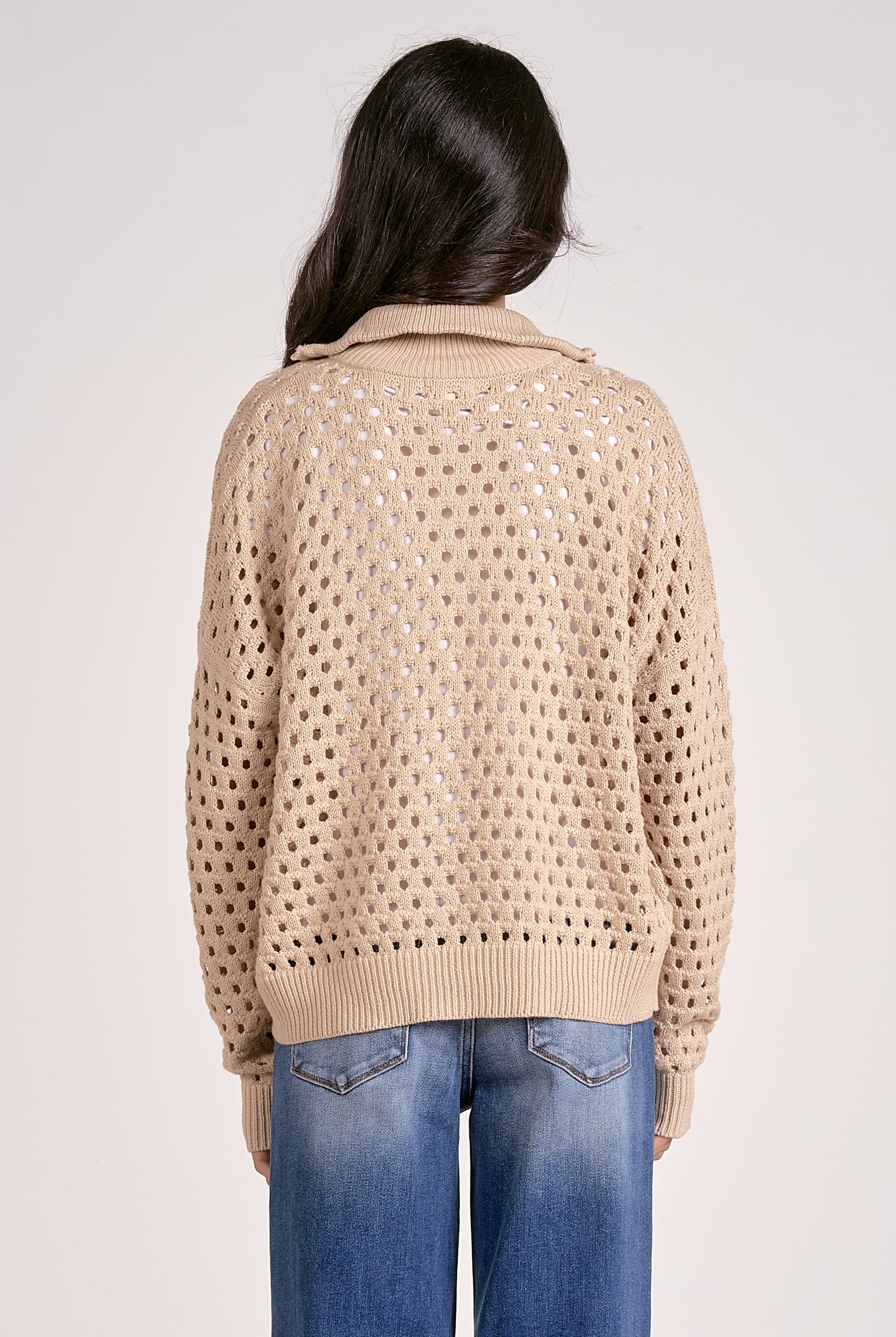 The back of a woman wearing a lightweight oatmeal half zip open knit sweater with ribbed cuffs and hem, styled with denim jeans.