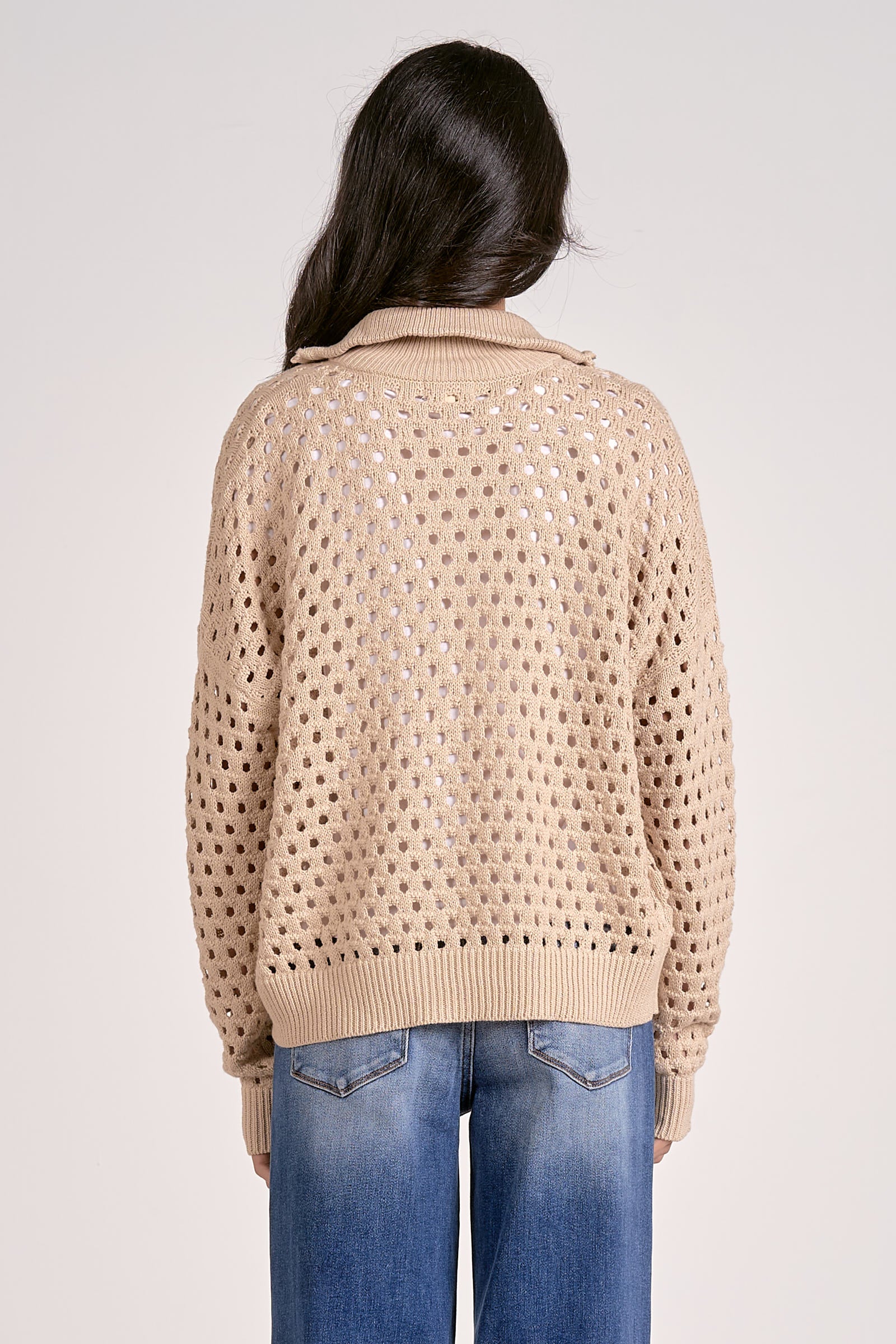 The back of a woman wearing a lightweight oatmeal half zip open knit sweater with ribbed cuffs and hem, styled with denim jeans.