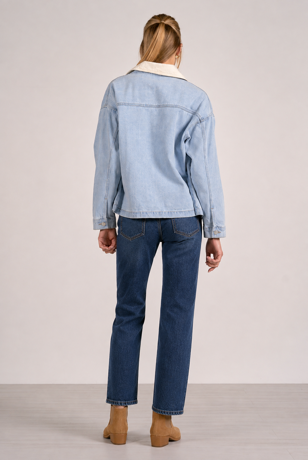 woman showing the back of the light blue denim jacket with contrasting cream colored collar.