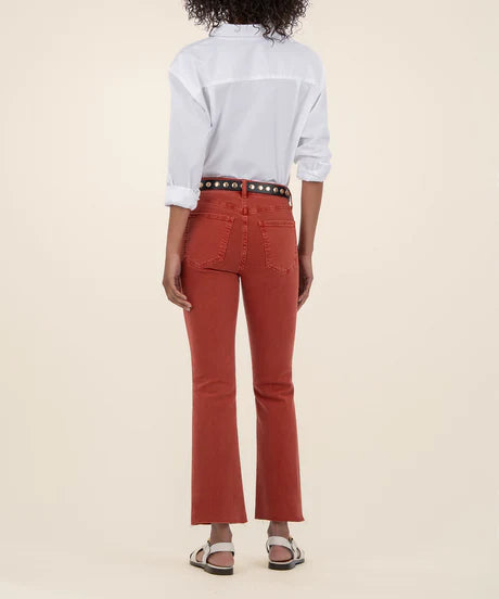 Woman showing the back of the high rise ankle flare jeans in the color paprika along with a white button down shirt and a black belt.