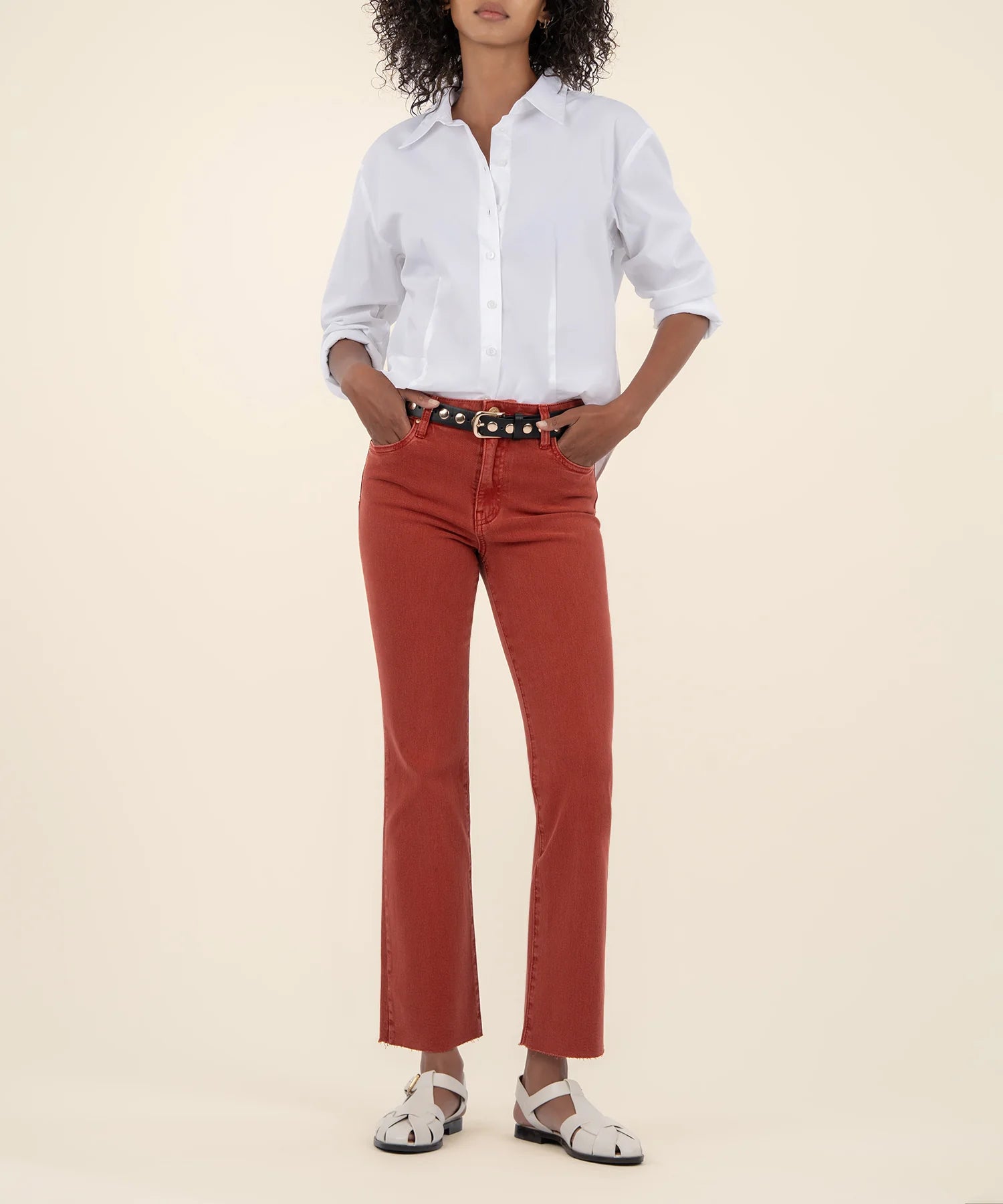 Woman wearing the high rise ankle flare jeans in the color paprika along with a white button down shirt and a black belt.