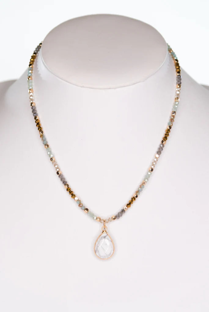 Multi-colored crystal bead necklace displayed on jewelry stand with marble teardrop pendant.