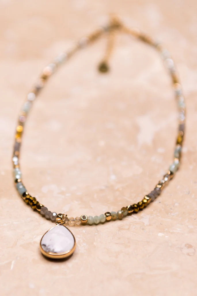 Multi-colored crystal bead necklace displayed on jewelry stand with marble teardrop pendant.