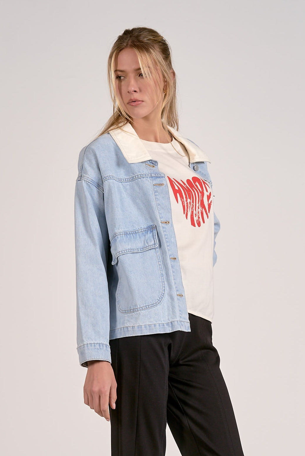 outfit view of light blue denim jacket styled with graphic tee and black pants.