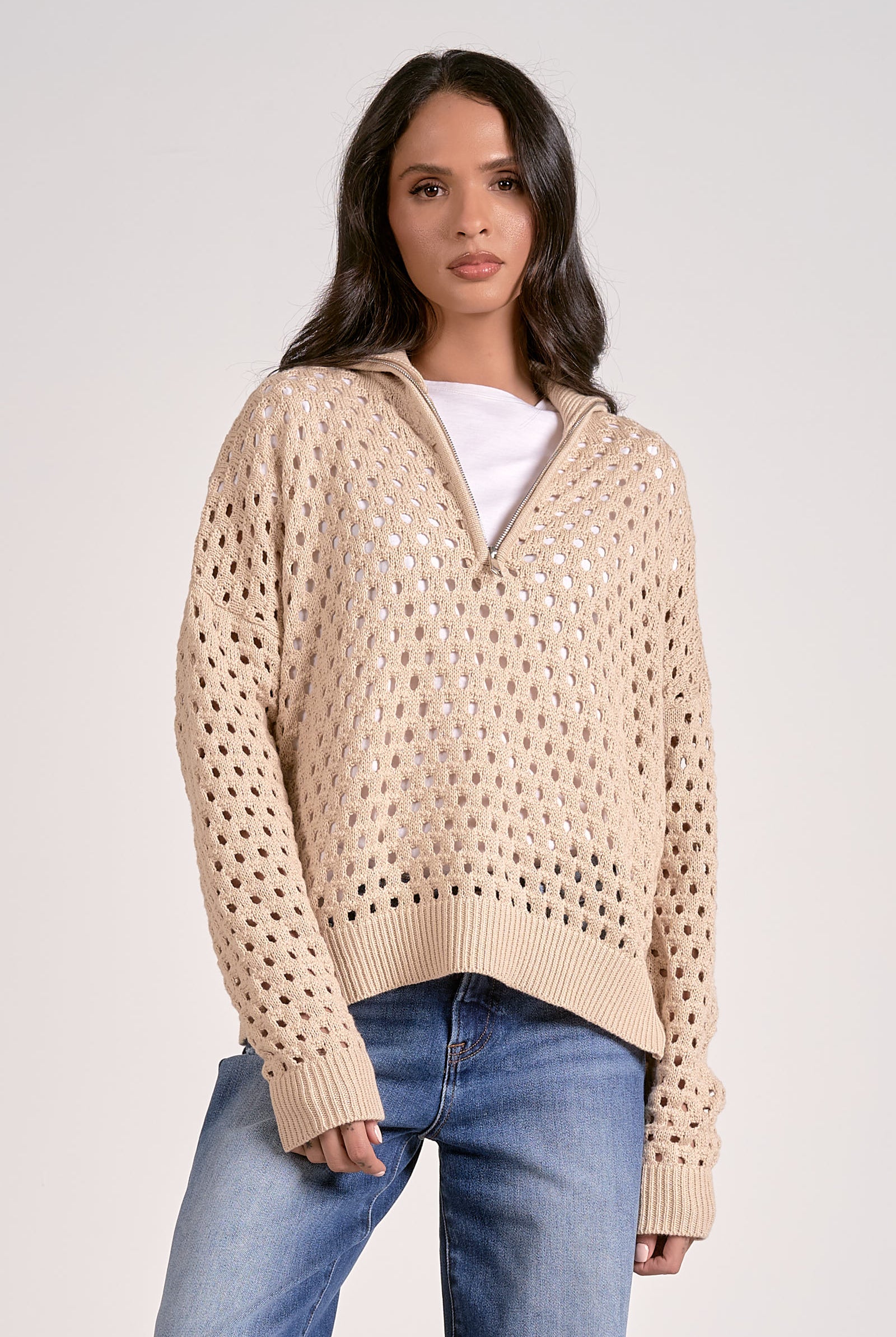 Woman wearing a lightweight oatmeal half zip open knit sweater with ribbed cuffs and hem, styled with denim jeans.
