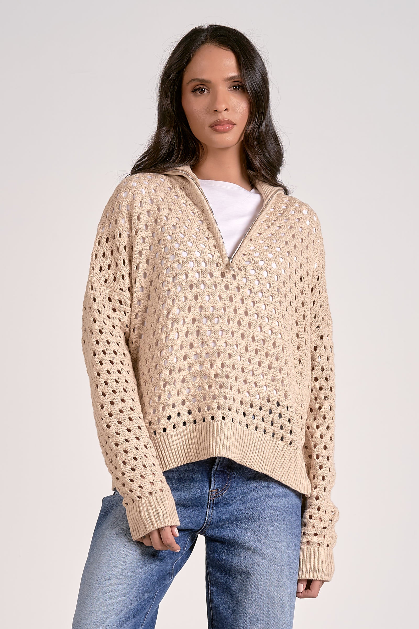 Woman wearing a lightweight oatmeal half zip open knit sweater with ribbed cuffs and hem, styled with denim jeans.