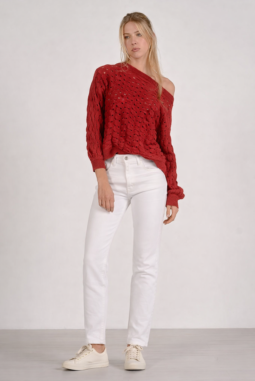 woman shown wearing red sweater off the shoulder with white denim