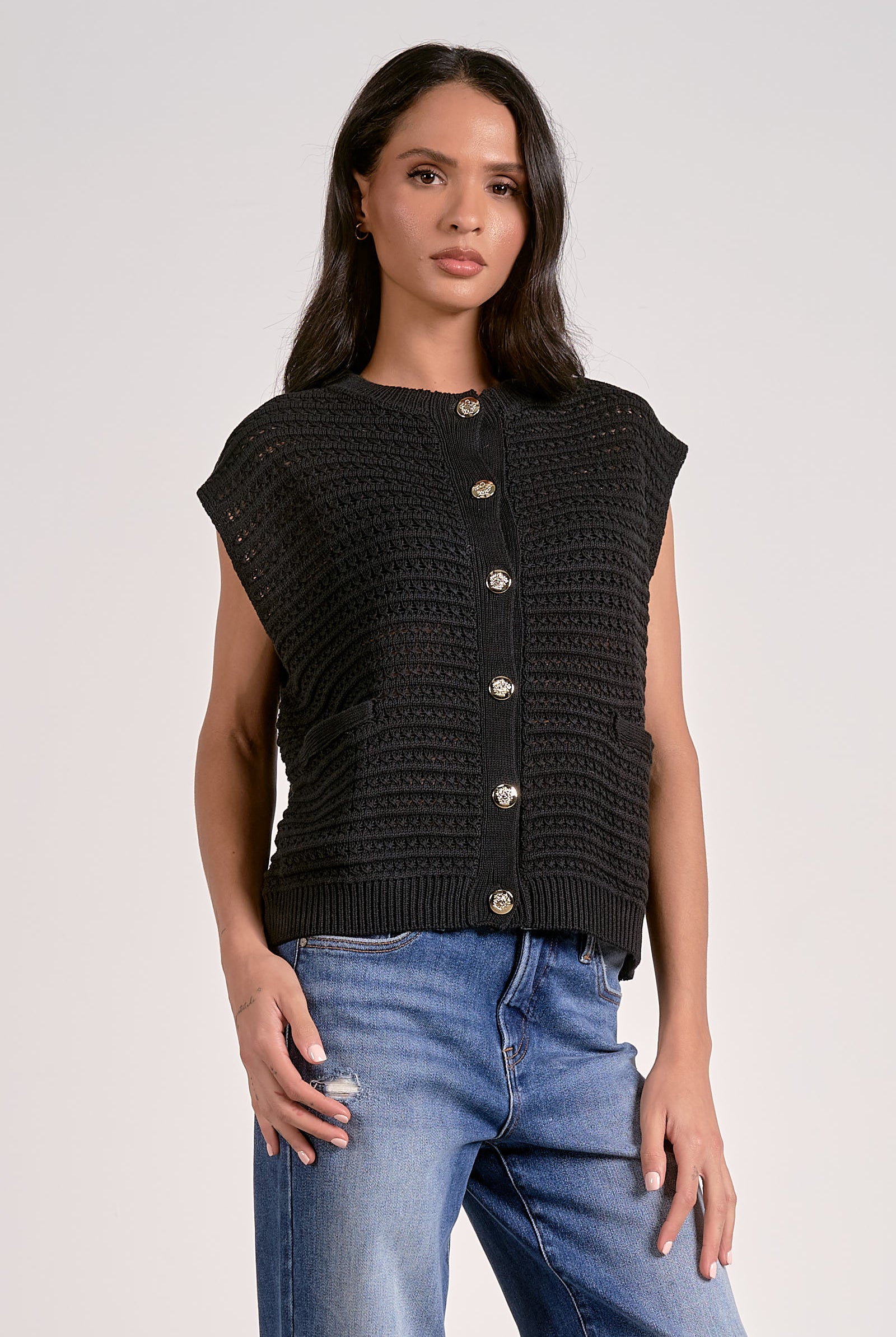 Model wearing black knitted cap sleeve vest with silver buttons, styled with denim jeans