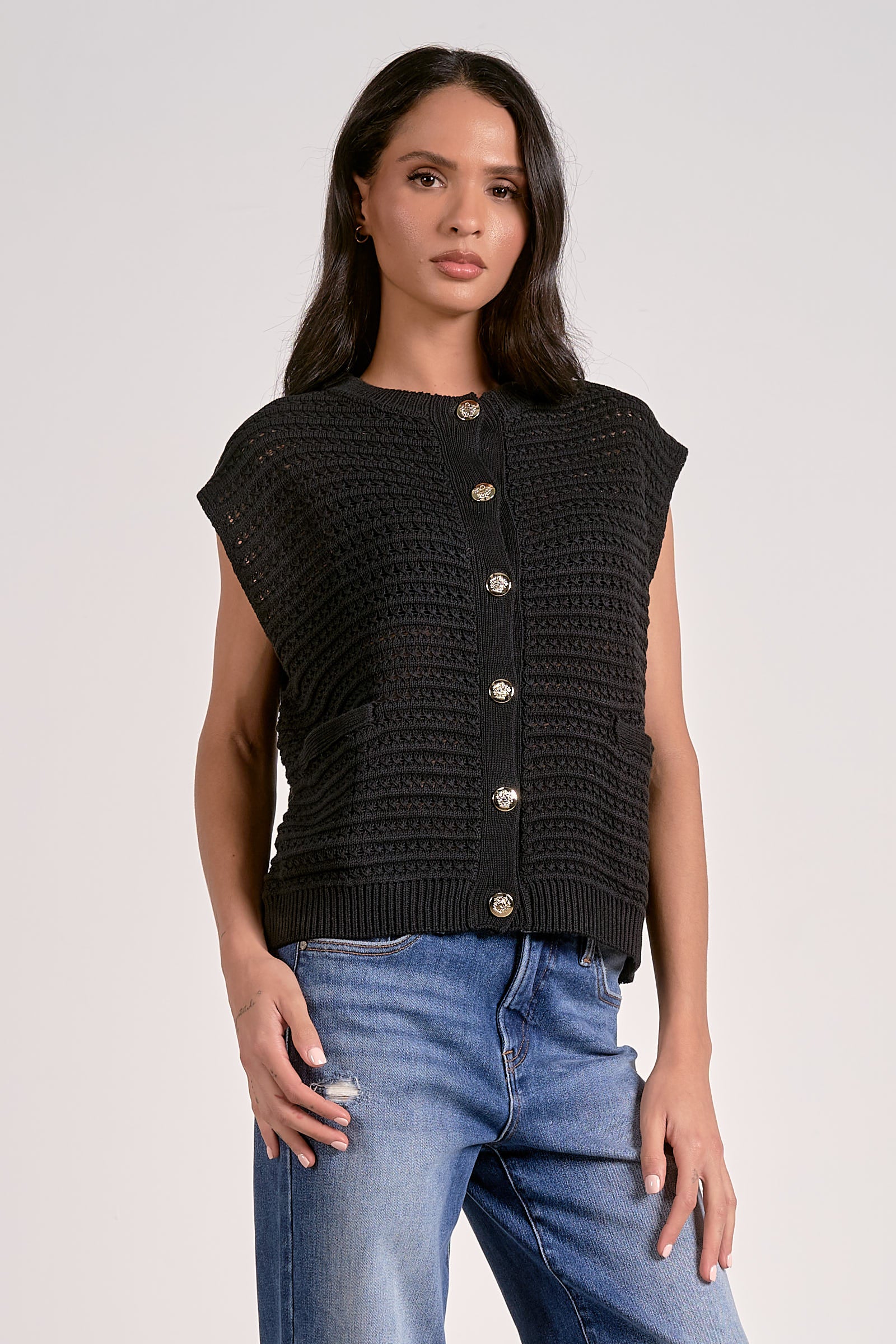 Model wearing black knitted cap sleeve vest with silver buttons, styled with denim jeans