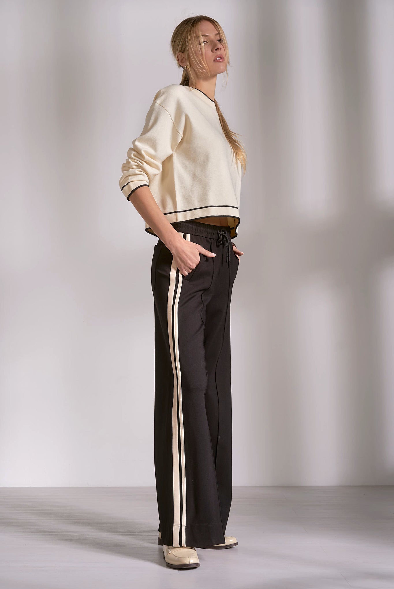 Side view of black track pants with natural stripe and fluid drape