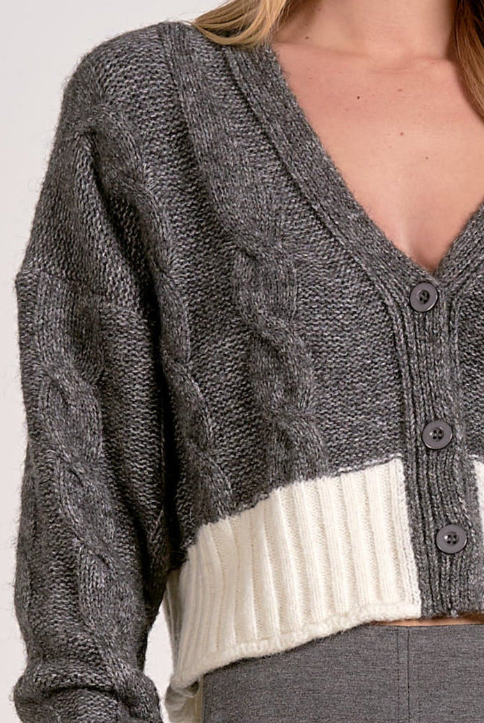 Close up view of the grey and white two-tone cropped v-neck cardigan with cable knit and button front