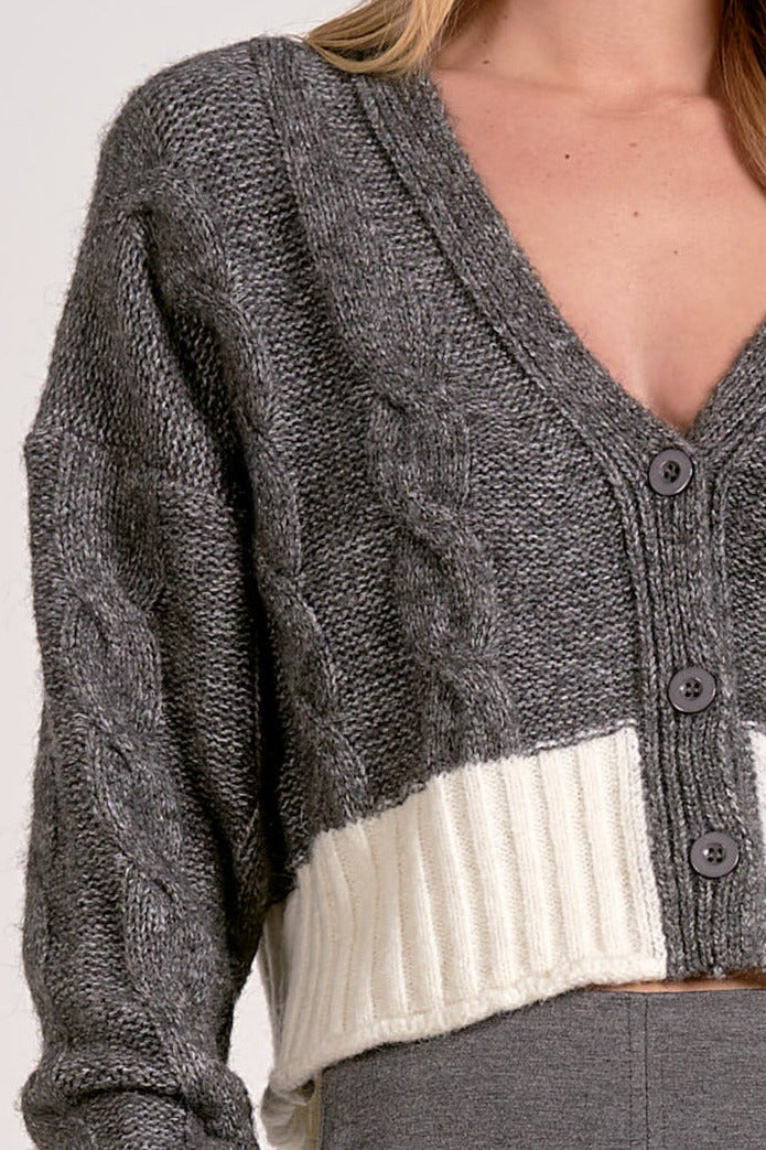 Close up view of the grey and white two-tone cropped v-neck cardigan with cable knit and button front