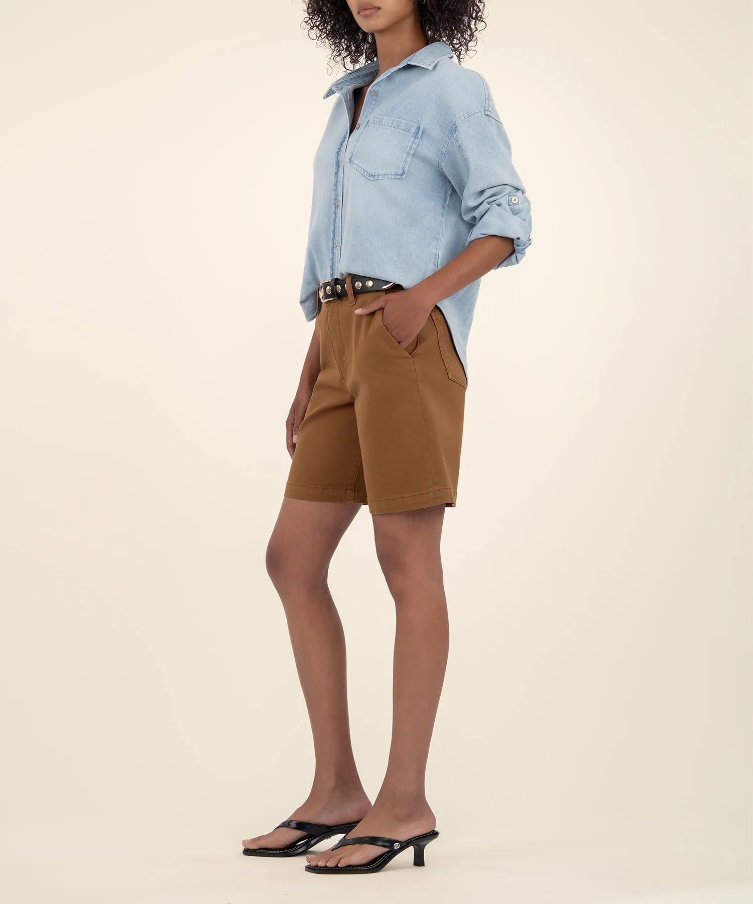 Person wearing a light blue denim shirt and brown shorts on a beige background