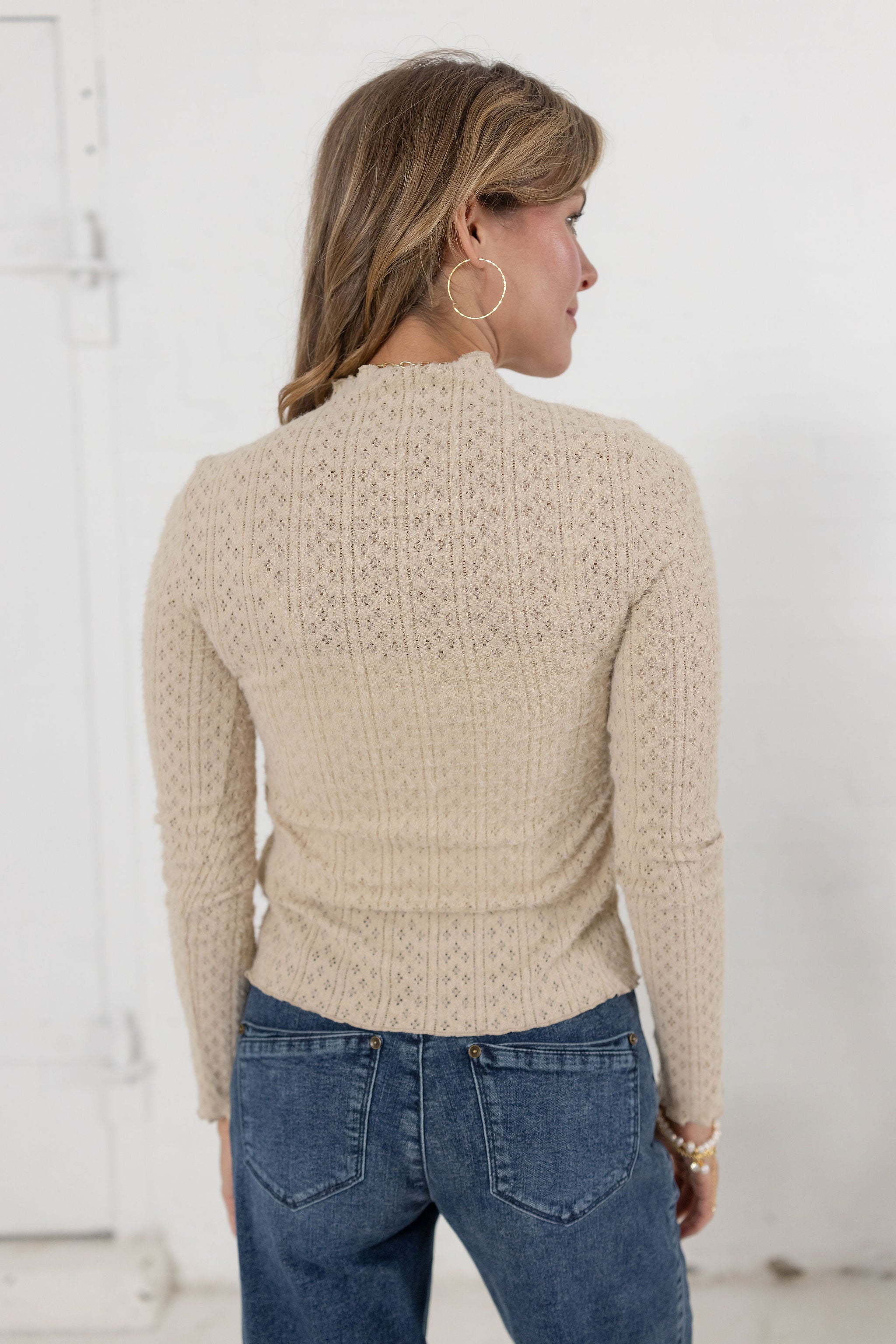 woman showing the back of the lettuce edge detail mock neck top in the color almond