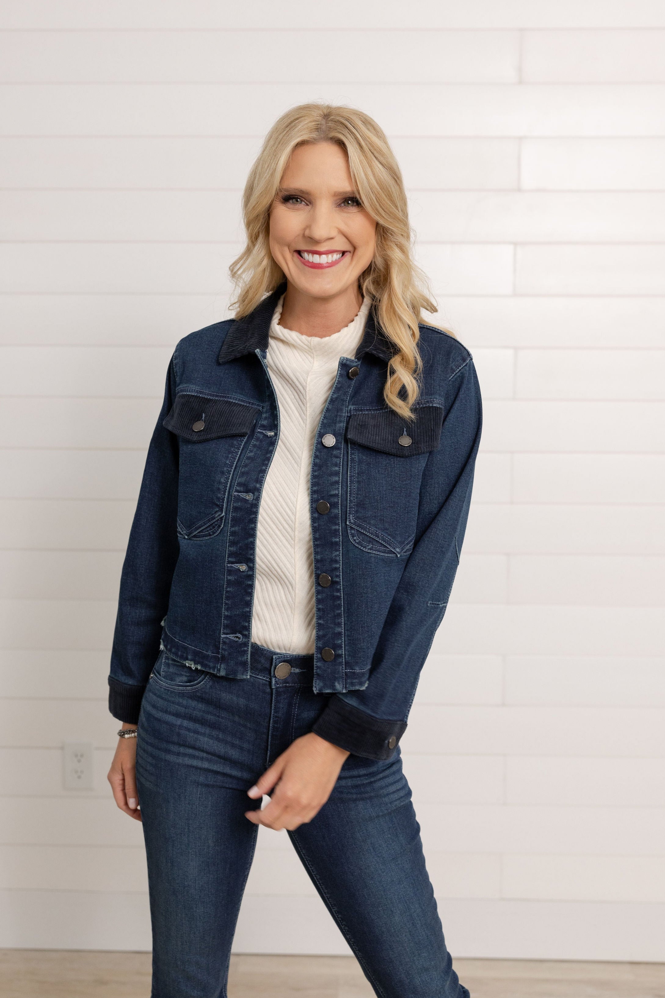 This is a woman moving around in a dark denim Mac and Me Jacket with Pockets and corduroy details.  She is also wearing the dark denim Mac and Me Boot Cut denim and the Mac and Me Funnel Tank Top in a cream color.  