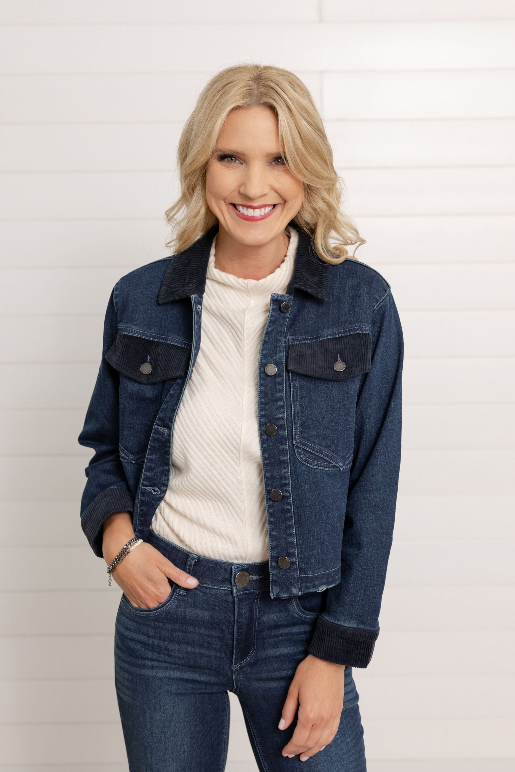A woman wearing a dark denim Mac and Me Jacket with Pockets and corduroy details.  She is also wearing the dark denim Mac and Me Boot Cut denim and the Mac and Me Funnel Tank Top in a cream color.