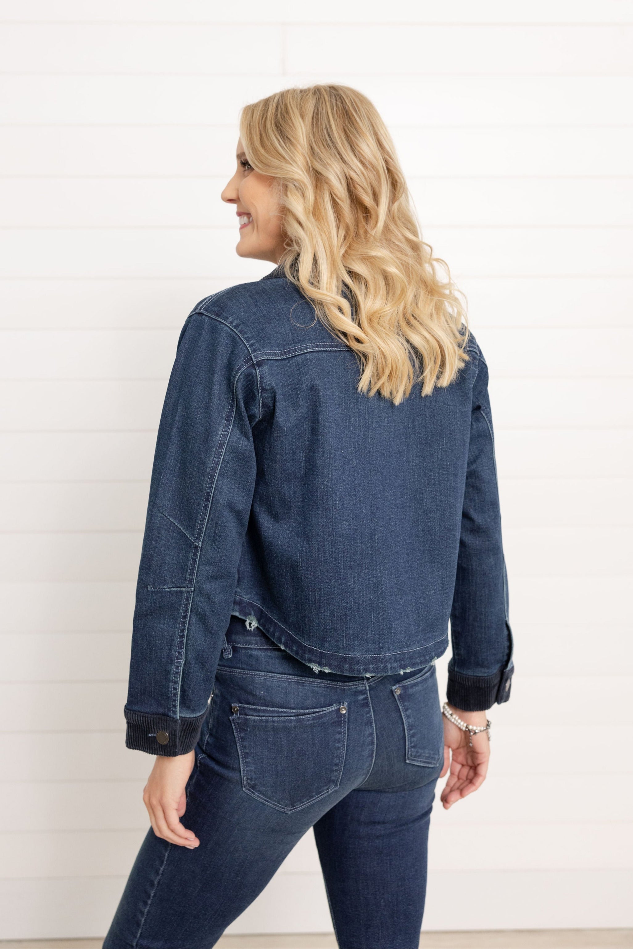 A woman wearing a dark denim Mac and Me Jacket with Pockets and corduroy details.  She is showing the back details of the jacket.