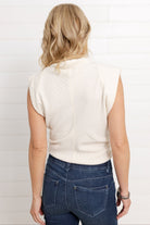 Model is wearing the Mac and Me funnel neck top and showing the back of the top.  It is sleeveless and has an extended shoulder for more coverage.  The color of the top is french vanilla and it creates a slimming effect with the ribbing placement.  