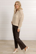A woman wearing a oatmeal colored open knit quarter zip sweater with brown pants at Mainstream Boutique Bloomington.
