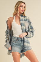Woman wearing a plaid shirt over a white top and denim shorts on a beige background