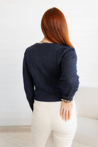 Woman wearing a Pointelle Cardigan knitted sweater and white pants against a light background