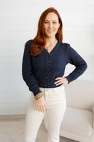 Woman wearing a Pointelle Cardigan with Rose Buttons and white pants in a minimalistic room.