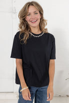 Model wearing The Soirée Tee in black with rhinestone embellished neckline from Mainstream Boutique Bloomington