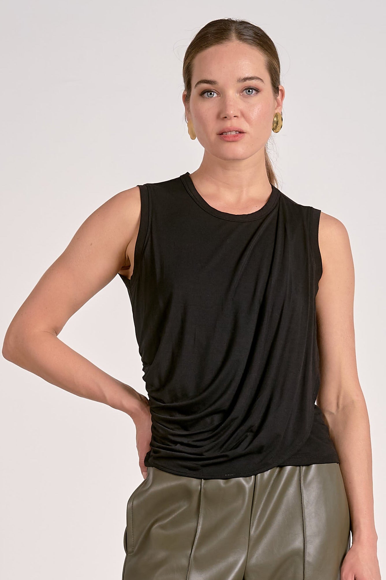 Woman wearing black draped sleeveless top with flattering side drape in a lightweight knit with leather pants