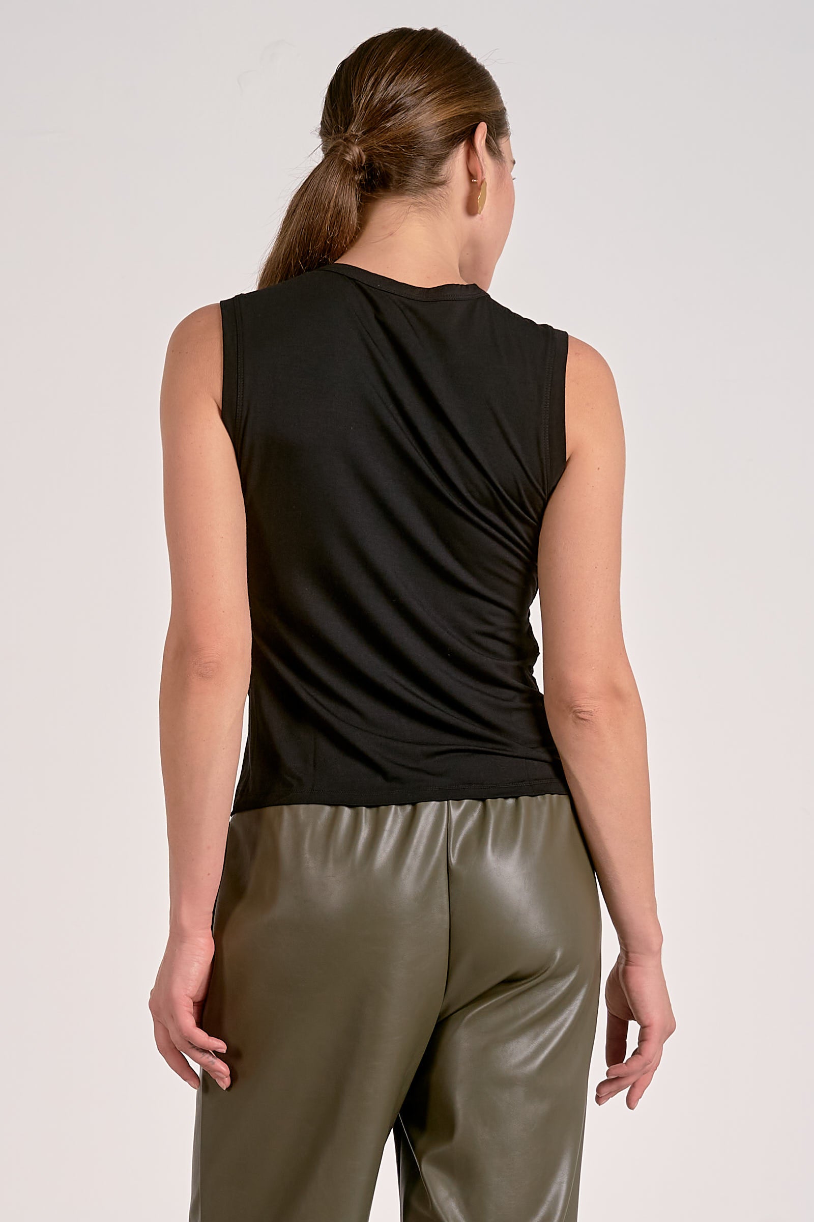 Woman showing back side of black draped sleeveless top with flattering side drape in a lightweight knit