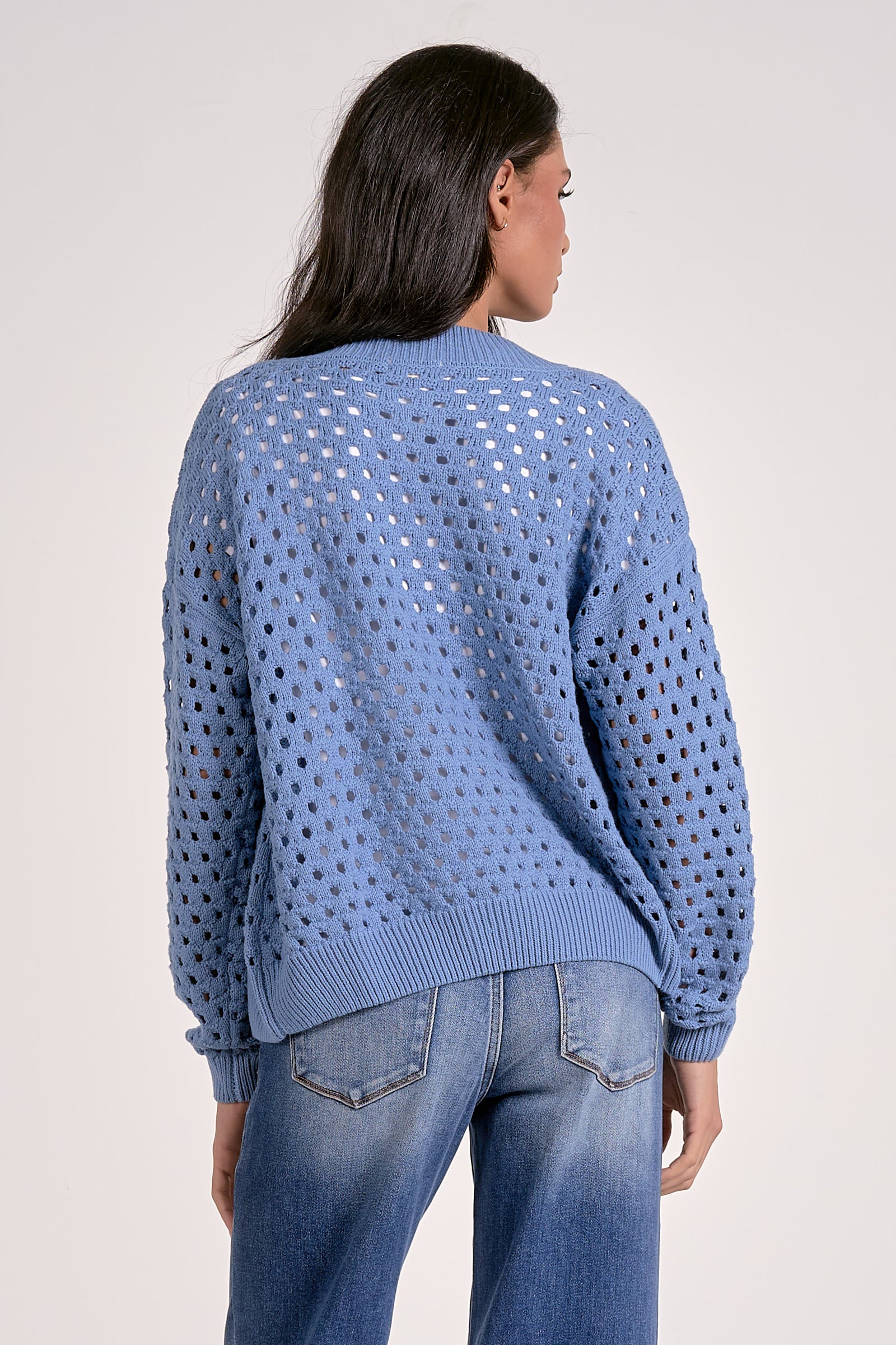 Woman showing the back of the soft blue open-knit zip cardigan layered over a white top.