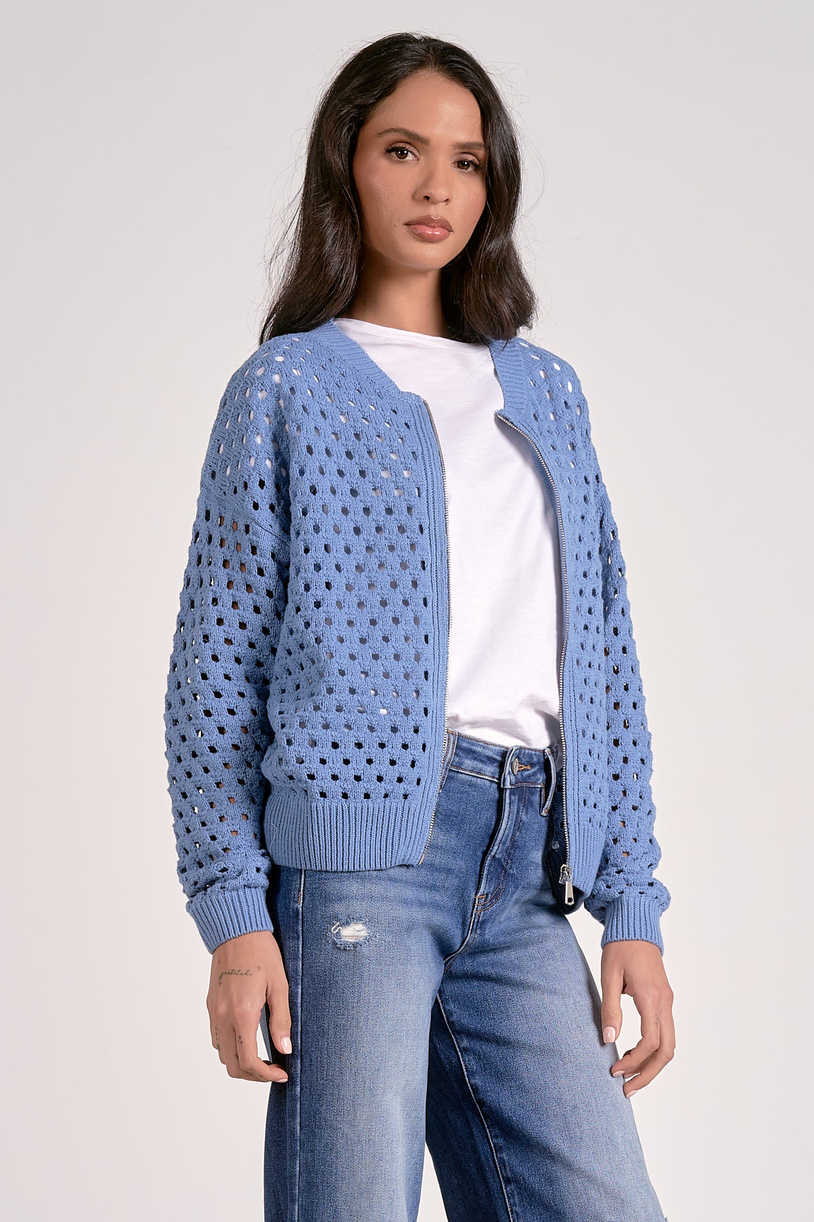 Woman wearing a soft blue open-knit zip cardigan layered over a white top.