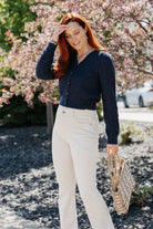 Woman in a Pointelle Cardigan with Rose Button and white pants standing in front of cherry blossom trees